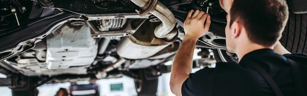 A GMC Service Center certified mechanic is inspecting a vehicle as it is raised above his head.